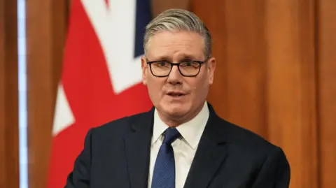 Sir Keir Starmer gives a news conference from a wood panelled room in front of a Union Jack.