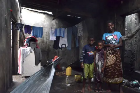 AFP A young boy, girl and a woman take shelter in a structure on 19 March 2019 surrounded by clothes and other belongings.