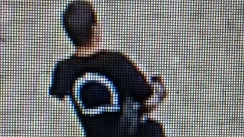 CCTV image of man wearing black T shirt with white circle