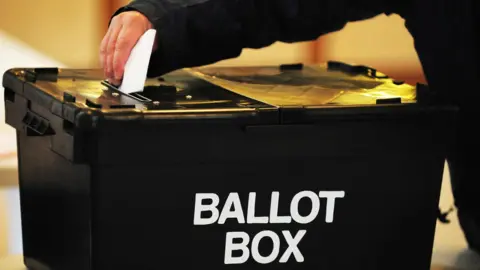 A voter places their vote into a black ballot box
