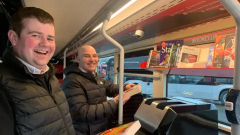 Matt Burley and Jason Asquith of Harrogate Bus Company holding books on the bus