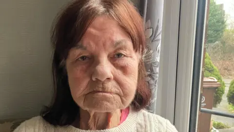 Richard Stead/BBC Maureen Parkisson has red hair with white roots and is wearing a white sweater