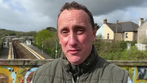 Andy Bowes-Roden looking at the camera. He is stood on a bridge above a train track.