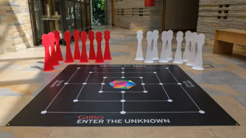 A large board game-style floor mat, with a slogan stating Games: Enter the Unknown, inside Lincoln Museum. In the background are giant board game pieces.