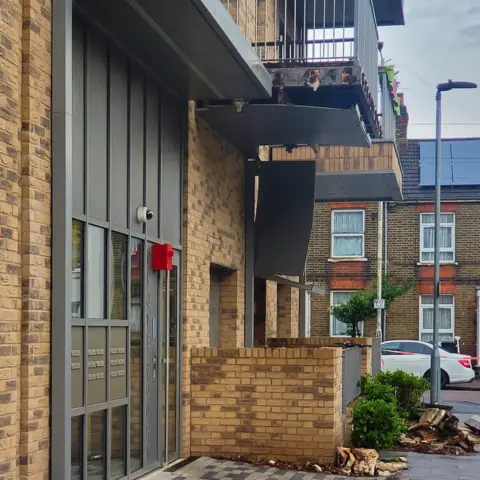 Base of a building showing broken timber and exposed metal from under a balcony