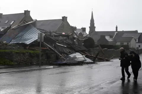 Getty Images Pedestrians walk past a destroyed warehouse in Porspoder, western France, on November 2, 2023