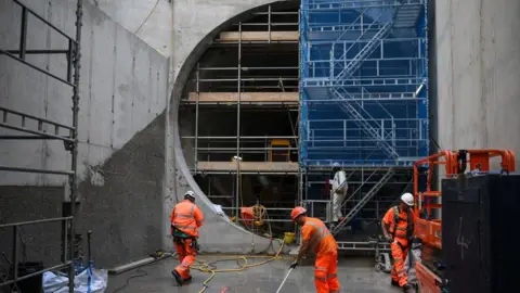 Getty Images A group of Thames Water workers in orange overalls are busy with various jobs next to a huge section of pipe that is under construction. 