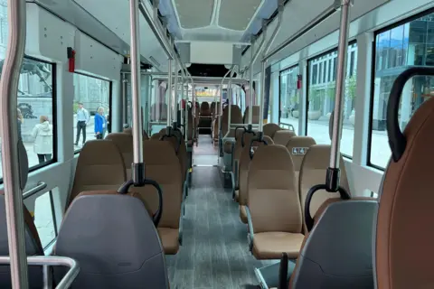 The interior of the bus. It has brown seats and many windows. It is a long vehicle. 