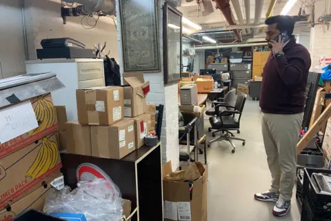 Danielle Kaye Vora takes a call in the basement of Concord Market, surrounded by cardboard boxes