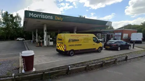 Street view of Morrisons Daily in Totnes with a yellow van and black car at the filling station
