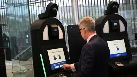 Getty Images A man with grey hair and wearing a dark suit is entering his personal details into a biometric machine. 