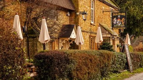 Getty Images Great Tew, Cotswolds, Oxfordshire, United Kingdom - stock photo. The front of a pub built with Cotswold stone.