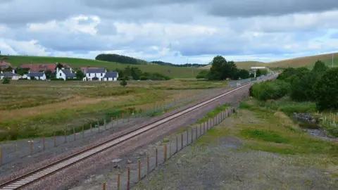 Jim Barton A railway line cuts through the Borders countryside under an ominous sky with a cluster of white houses to the left