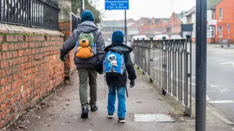 Two boys with backpacks pictured from the back walking forward on a pavement 