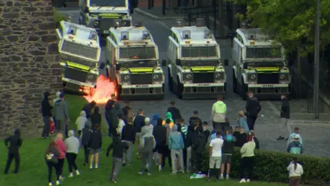 BBC Trouble em Londonderry mostra cinco Land Rovers, um deles em chamas, após um ataque criminoso a um bombardeiro a gasolina