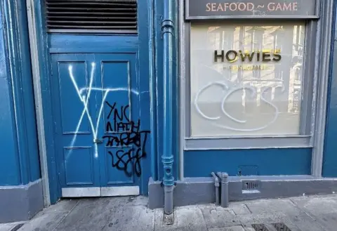 Andrew McRae There is white and black graffiti on the blue door of the restaurant.