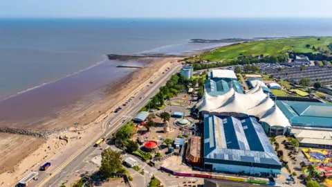 A birds-eye view of Butlins in Minehead by the seafront. There are big buildings and some tents. It is sunny and the coastline is visible