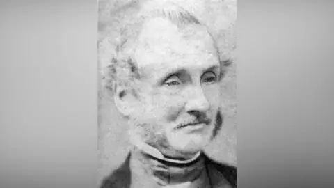 Black and white portrait of William Marwood he has grey short hair, moustache and sideburns with stiff collar and black jacket