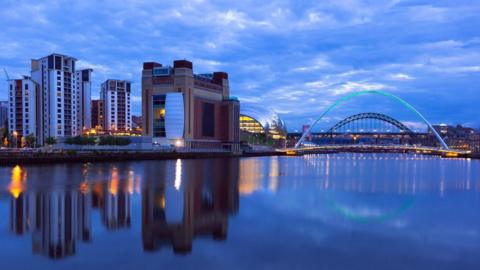 Night-time picture of the quayside in Newcastle looking across to Gateshead with the Millennium Bridge and Tyne Bridge in the background