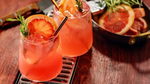 Two pink cocktails with grapefruit and rosemary, in short glasses with metal straws