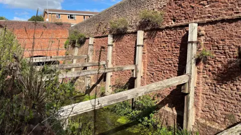 Canal & River Trust Albert Street Cutting in Bridgwater. There are only wooden boards left, which are connected to a red brick wall by the canal.