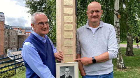 Philip and Peter Rowe holding a framed photo of their father at the memorial.