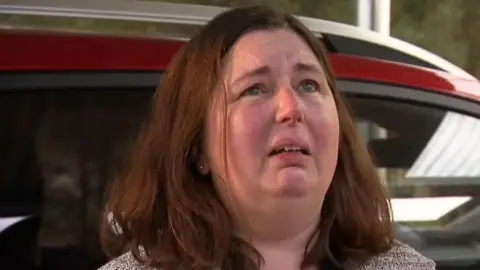 Headshot of Erin Patterson as she looks up while stood in front of a car