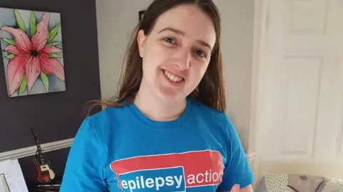 Supplied A smiley woman with dark hair wears a blue t-shirt with 'epilepsy action' on the front