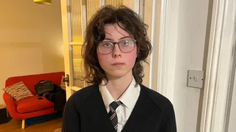 A 16 -year -old girl with a neutral expression Qays Najm/BBC portrait photo, with a neutral expression and wearing her Refam High School uniform. 