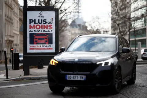 Reuters An SUV melewati poster di Paris mempublikasikan pemungutan suara pada tahun 2024 karena meningkatkan biaya parkir untuk mengurangi emisi dan meningkatkan keselamatan pejalan kaki