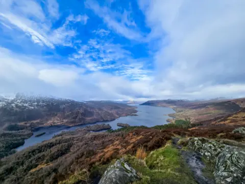 Nicola Orr A view of a loch taken from a hill with blue sky above