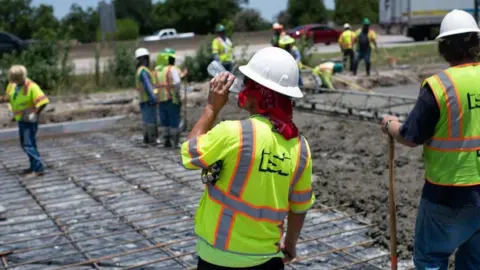 A construction worker takes a sip of water while repairing a road that was damaged from the heat in Houston, Texas on June 27, 2023.