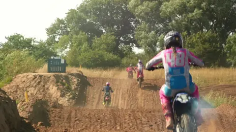 Four young motocross riders drive over a dusty track with speed bumps.
