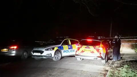 Dan Jessop Two police cars next to a crashed Citroen Berlingo, with police tape surrounding it and two officers beside the patrol cars, in the dark.