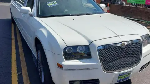 TVP Roads Policing A white limousine, with police stickers on it, parked up by double yellow lines. 