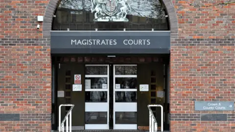 Front of a court building entrance. There are sliding doors. In front of them are steps. A sign on the right says 'Crown & County Courts' 