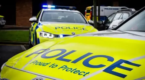A generic picture of yellow police cars and a van in the background.