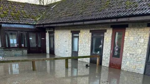 World Horse Welfare A flooded walkway outside a pale brick building with a brown roof.