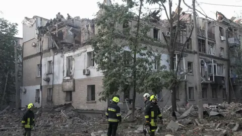 Reuters Firefighters stand atop and around a destroyed apartment building in Dnipro, Ukraine after a series of overnight Russian strikes.