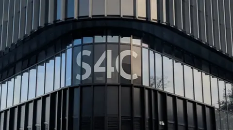 The exterior building of S4C. It is black panelled with vertical windows and the word S4C in white font. 