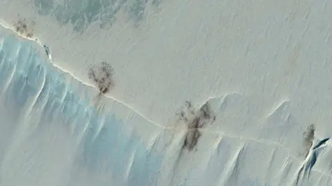 Vantor Una imagen satelital del hielo marino que muestra una extensión de color blanco con pequeñas manchas marrones.