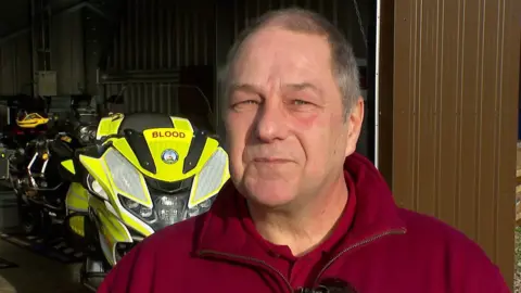 Steve Dower, Chairman of South West Blood bikes standing in front of a motorcycle.
