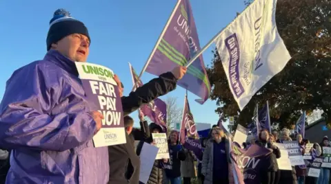 A crowd of picketing workers holding signs outside a school in Perth