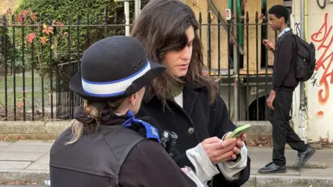 Getty Images A police officer speaks to a woman looking at her phone whilst walking through Clissold Park in Hackney