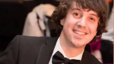 Family handout Oliver Robinson smiles at the camera wearing a black tuxedo and bow tie. His hair is mid-length and brown. 