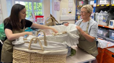 Two volunteers pack Moses baskets with essential supplies