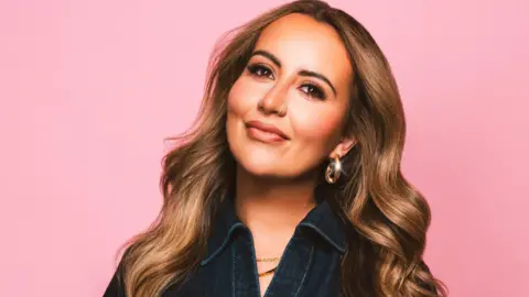 BBC Sophie Gravia has long brown hair. She is smiling as she poses against a pink background.