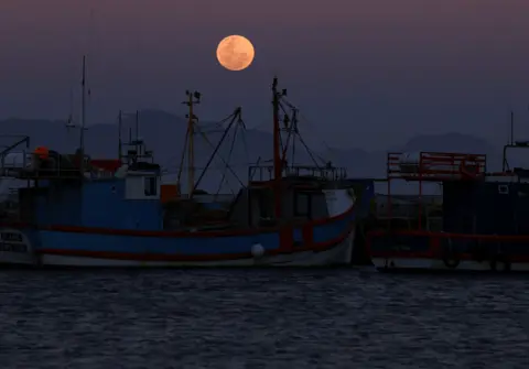 ESA ALEXANDER / REUTERS Bulan super, yang dikenal sebagai Bulan Biru, terbit di atas pelabuhan Kalk Bay di Cape Town. 