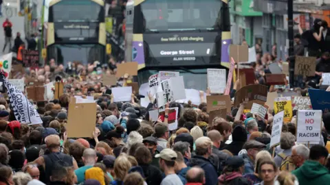 EDDIE MITCHELL Anti-racism demonstrators hold placards as two buses are held up on Queens Road