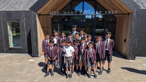 A group of children standing together in navy and red school uniforms.